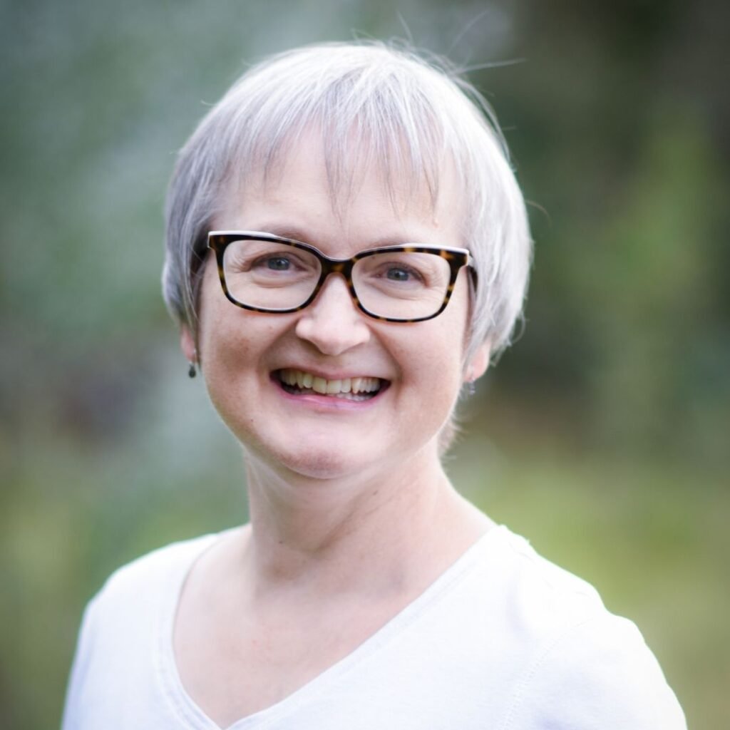 Julie Behnken smiling wearing a white v-neck shirt. blurred outside background